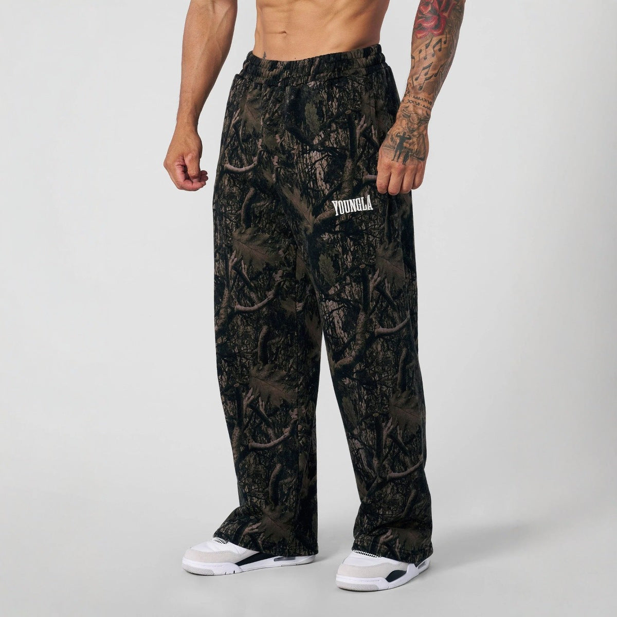 Person wearing camouflage pants with a brand logo on a plain background